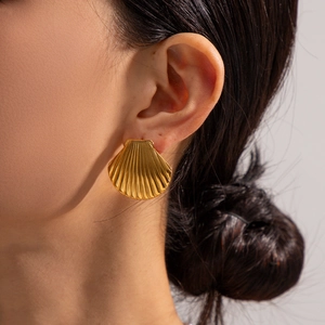 Macro detail of golden seashell earrings showing intricate 3D radial textures on model