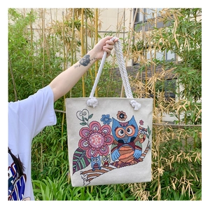 Detail of colorful owl embroidery on beige canvas tote bag with white rope handles