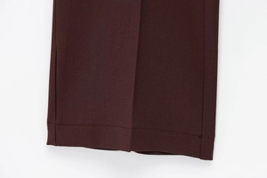 Gros plan d'un pantalon bordeaux montrant la texture sergé et les coutures de l'ourlet