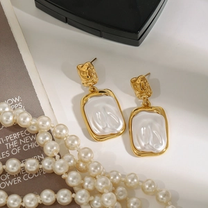 Elegant gold square stud earrings with pearl-like texture on a minimalist white table