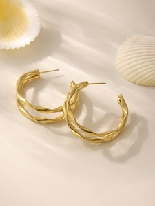 Gros plan de boucles d'oreilles créoles torsadées dorées à double couche sur un coquillage