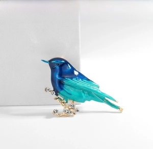 Detail of bird brooch with blue gradient enamel and rhinestones on a white background