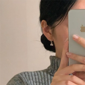 Detail shot of a silver 925 pearl drop earring on model wearing grey turtleneck