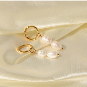 Detailed shot of golden baroque pearl hoop earrings on soft beige silk fabric