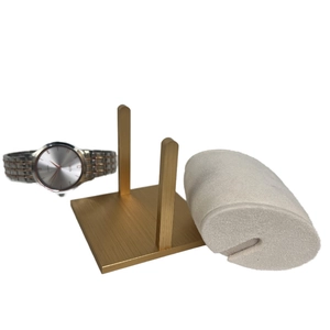 Detailed view of a metal watch display stand with a soft beige velvet pillow and gold base
