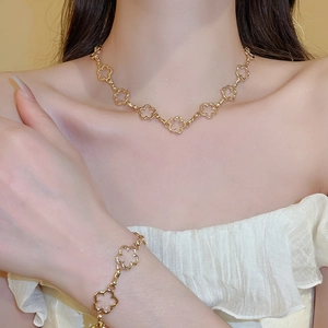 Detail of a model wearing a gold flower clover necklace and bracelet jewelry set