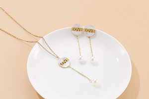 Detailed close-up of gold necklace and pearl earrings with shell LOVE pendants