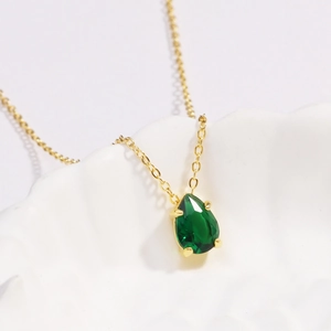 Elegant gold necklace with a pear-shaped emerald pendant displayed on a textured plate