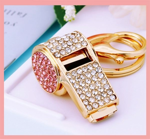 Detail of gold metal whistle keychain with white and pink crystal rhinestones