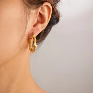 Close-up of elegant gold twisted hoop earring worn by a model on a beige background