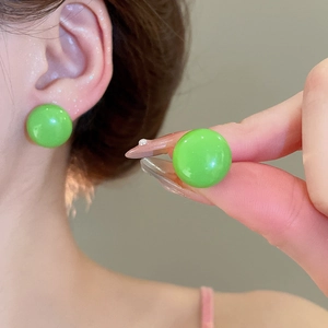 Detail view of a glossy vibrant green ball earring on ear with high-shine finish