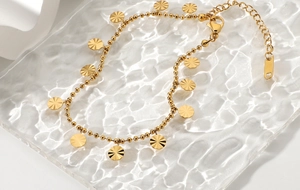 Detailed macro view of 18K gold plated beaded anklet with sunburst disc charms on glass