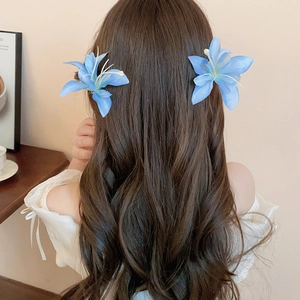 Detail of blue hibiscus fabric flower hair clips worn on wavy dark hair for a vacation look