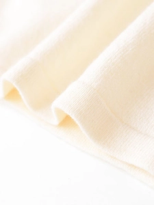 Detailed close-up of ribbed texture and soft pure wool fabric on a beige knit top