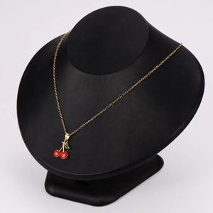 Elegant gold chain necklace featuring red cherry and green leaf pendant on a black bust stand