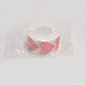 Detail view of heart-shaped pink sticker roll in transparent packaging on white background