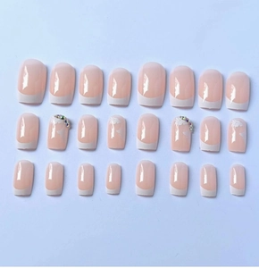 Detail of nude pink French press-on nails with white floral patterns and rhinestones
