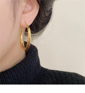 Close-up of elegant gold twisted hoop earrings with woven texture on a model wearing black