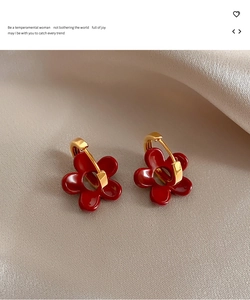 Détail macro de boucles d'oreilles fleurs rouges et anneau doré sur soie beige