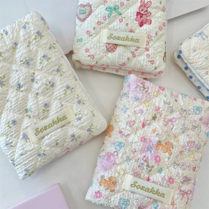 Close-up of quilted floral and animal pattern fabric pouches with gold logo embroidery