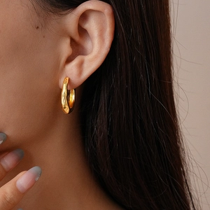 Close-up of golden geometric pleated hoop earring with textured metallic finish on model