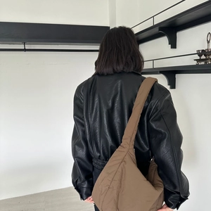 Close-up of a brown padded puffer crossbody bag styled with a black leather jacket