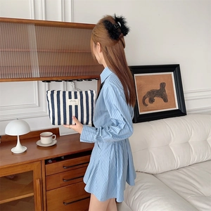 Close-up of blue and white striped canvas toiletry bag held by a model in a lifestyle setting