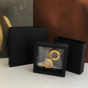 Close-up of golden textured earrings inside a sleek black floating jewelry display box