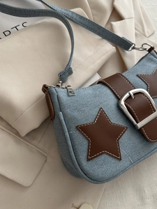Detail of blue denim hobo bag with brown star patch and large silver metal buckle strap
