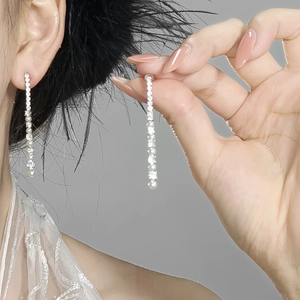 Close-up of elegant long tassel earrings with sparkling zircons and delicate pearls
