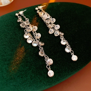 Macro shot of sparkling zircon tassel earrings on green velvet pad with luxury finish