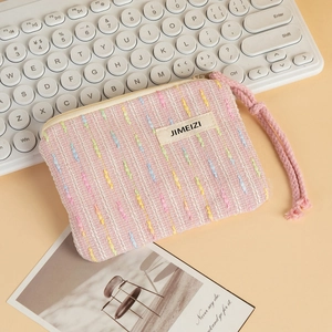 Close-up of pink tweed coin purse with zipper and wrist strap on beige surface