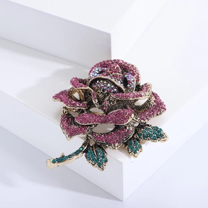 Macro shot of vintage gold rose brooch with pink and green rhinestones on white block