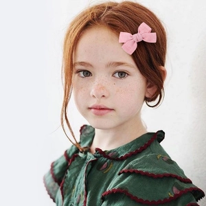 Detailed view of a small pink fabric bow hair clip worn by a girl with red hair