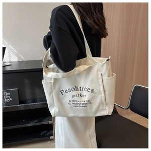 Detailed view of cream canvas tote bag with black graphic text print worn on shoulder