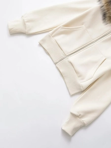 Detail of detachable fur collar and ribbed cuffs on off-white zip-up hooded sweatshirt