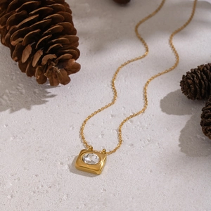 Detail of 18K gold plated necklace with oval zircon pendant on stone surface