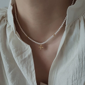 Close-up of elegant pearl necklace featuring a golden cross pendant on a white shirt