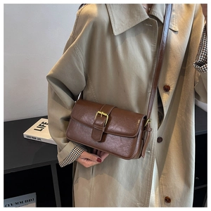 Close-up of brown vintage wax leather crossbody bag worn with a classic beige trench coat