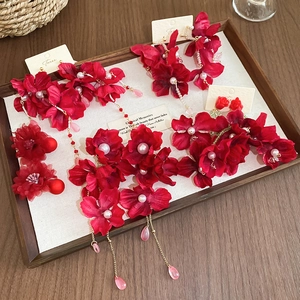 Close-up of red fabric floral earrings with pearl beads and gold tassels on a wooden tray