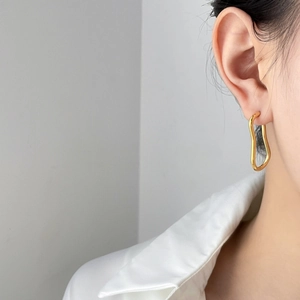 Close-up of model wearing gold abstract wavy hoop earrings with minimalist geometry