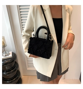 Close-up of a black quilted tote bag with round handles on a model in a white suit
