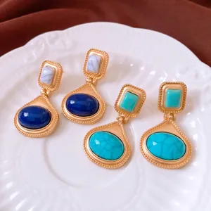 Vintage gold oval earrings with blue and turquoise stones on ceramic plate