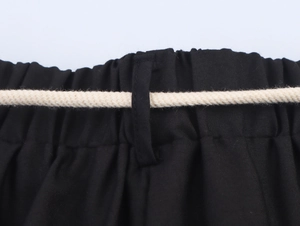 Dettaglio dei pantaloni ricamati neri con vita elastica e cintura in corda intrecciata