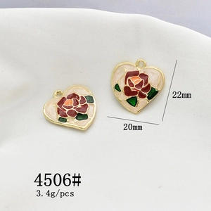 Macro shot of gold heart-shaped pendants with white enamel and red rose details