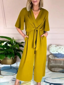 Detail of V-neck mustard yellow jumpsuit with waist tie and textured woven fabric