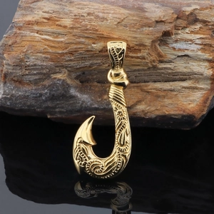 Detailed view of a golden fish hook pendant with engraved texture on a dark surface