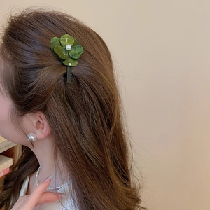Détail d'une pince à cheveux fleur verte en résine avec perle sur cheveux bruns