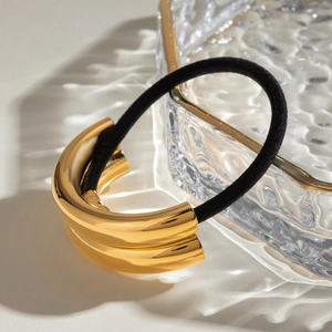 Minimalist gold metal hair tie with black elastic cord on water ripple glass tray