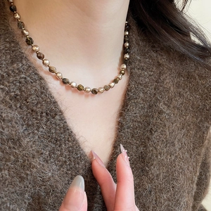 Macro detail of tiger eye beaded necklace on brown sweater showing vintage aesthetic